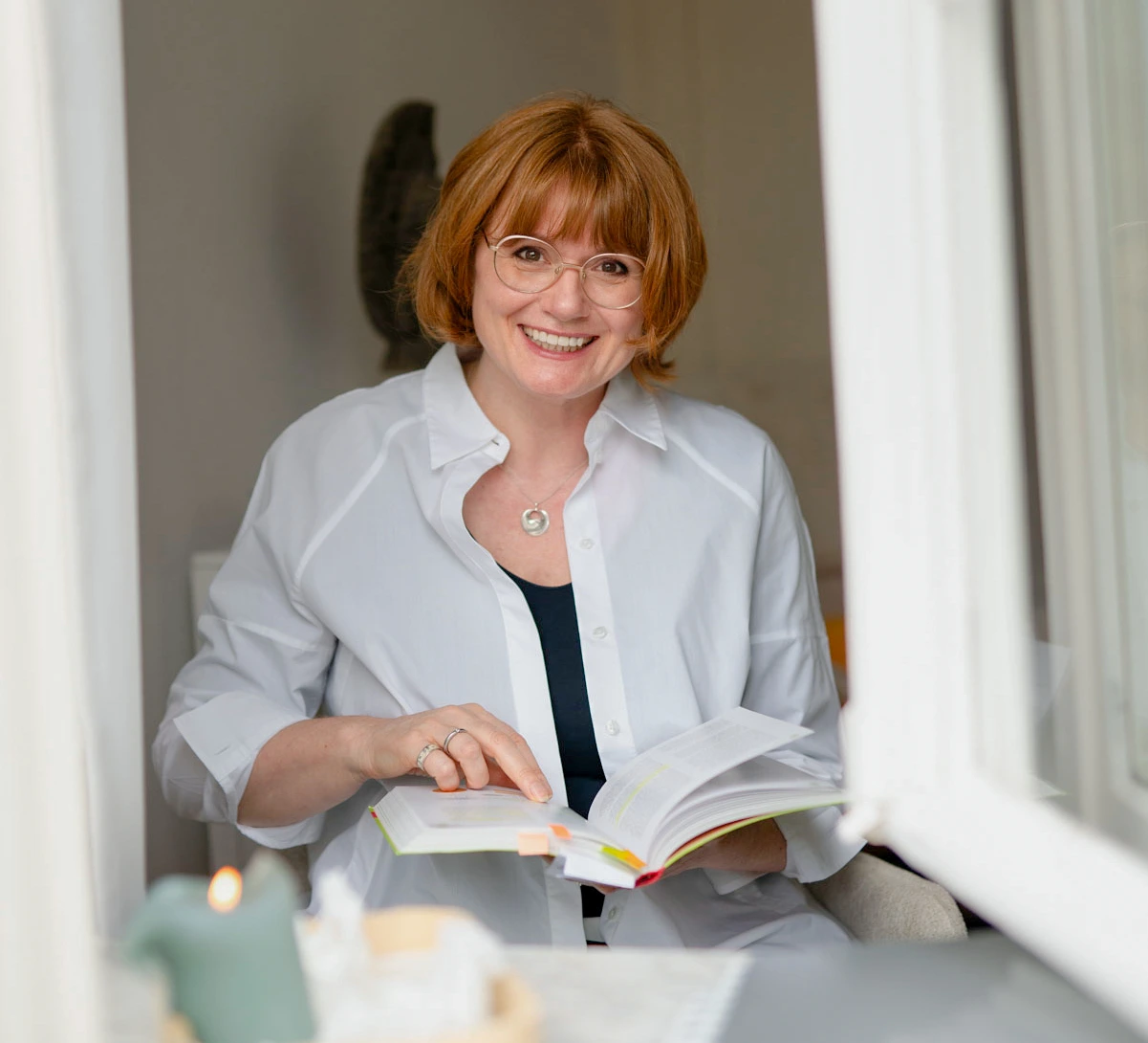 Frau mit Buch schaut aus einem Fenster